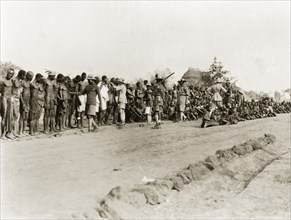 Sleeping sickness inspection. Sudanese men and boys stand and sit in a line on a roadside awaiting