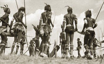 Sudanese warrior costume. A group of Sudanese men gather in a circle holding spears and drums. They
