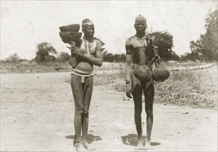 Dinkas on a country road. A young Dinka man and woman carry bowls and gourds on a country road.