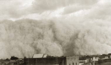 Sudanese sandstorm. A giant cloud of sand engulfs a townscape during a sandstorm. Sudan, circa 1925