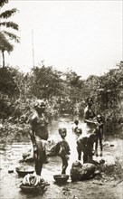 River laundry. A group of half-naked African women and children wash clothes in a shallow river
