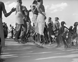 Turkana dancers mid-jump. Turkana adults and children wearing traditional dress are captured