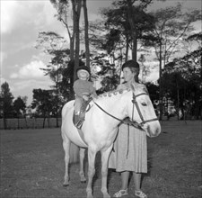 Children's pony riding. A woman smiles at a small child who sits proudly astride a white pony