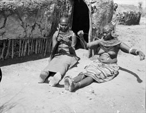 Samburu women threading beads. Two Samburu women sit outside a mud hut threading beads onto long