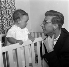 Peter Murdock and his baby. Peter Murdock's baby holds onto the side of a cot, gazing into the eyes