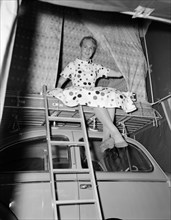 Girl in a spotted dress. A young woman in a spotted dress sits, ankles crossed, on a padded rack