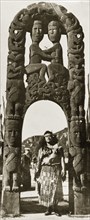 Beneath a Maori arch. A Maori woman in traditional dress stands beneath an ornate Maori arch that