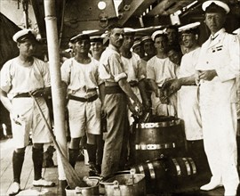 Grog and lime juice. Uniformed sailors aboard a British Special Service Squadron warship queue to