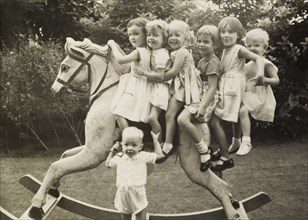Alison's birthday party. Six smiling young girls sit astride a large rocking horse at 'Alison's