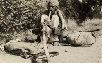 Snake charmer. A turbaned snake charmer crouches low on the ground as he attempts to charm a cobra