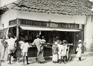 Tanganyika street shop. People wait to be served from a busy market stall housed in a ramshackle