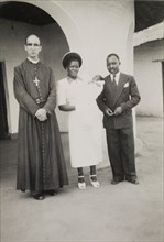 After the christening. A proud African couple pose beside a European priest following the