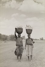 Transporting vegetables. A man and a woman walk along a dusty road balancing baskets full of