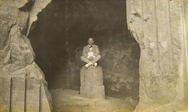 Inside the Elephanta Caves. A European man sits cross-legged, posing for the camera on a stone