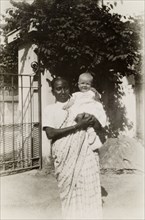 Ayah with baby. An Indian ayah (nursemaid) holds a British baby outside the gates of a colonial