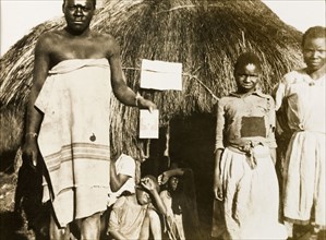 African worker with children at Balloch Farm. An African farm worker holds up a piece of paper or