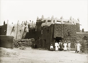 An ancient Hausa building in Kano. A number of Nigerian men stand outside a mud-walled building,