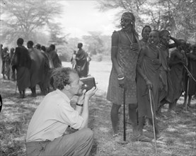 Filming Maasai dancers. A European man identified as 'Johnson' crouches down to take a photograph