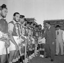 The 1956 Kenyan Olympic hockey team. A suited official shakes hands with a line up of players from