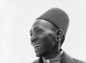 Kikuyu man. Portrait of a smiling Kikuyu man in shirt, jacket and fez-like hat. The photograph does