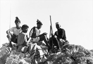 Kikuyu Home Guards on patrol. Four Kikuyu Home Guards on patrol sit atop a rocky outcrop. One wears