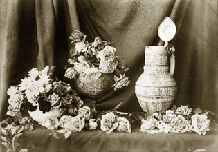 Still life composition, Australia. Roses and daisies spill out around two bowls and an ornate jug,