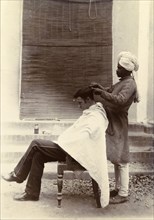 Cut your hair Sir'. A turbaned Indian barber trims the hair of a British gentleman who sits