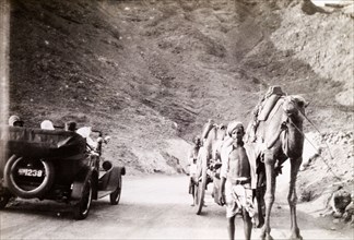 Road traffic near Suez. An Egyptian man leads a camel and cart along a winding road past a motorcar