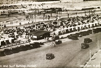 The seafront at Durban. Motorcars line the seafront at Durban. Crowds of people with parasols pack