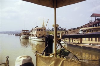 Lokoja trading houses and ferries. Two large ferries docked on the riverside near the Royal Niger