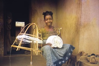 Spinning thread, Nigeria. A young woman sits beside a homemade spinning frame, a bundle of cloth