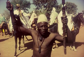 Celebrating the end of Ramadan. A barechested Nigerian man poses for the camera, waving two sticks