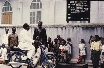 Pastor on a moped. Reverend J. Harwood, a Church of Nigeria pastor, pulls over his moped to chat