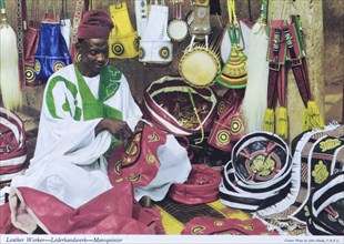 A leather craftsman, Nigeria. A colourful tourist postcard depicts a Nigerian leather craftsman at