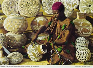 Carving calabashes, Nigeria. A colourful tourist postcard depicts a Nigerian craftsman at work,