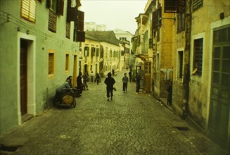 Street scene in Macau. People go about their daily business on a cobbled street bordered by