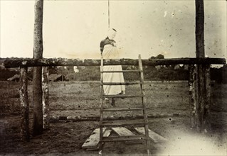 Colonial execution of a woman. The body of an African woman hangs by the neck from a wooden