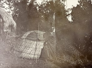 Wickerwork village hut. A Kenyan man and child stand are pictured in their village beside a