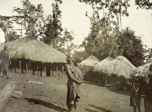 Domestic village scene, Kikuyu. Domestic village scene. A Kikuyu woman wearing traditional dress