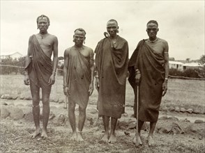 Four Kikuyu men. Group portrait of four Kikuyu men wearing traditional dress and jewellery. British
