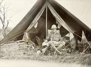 Geoffrey Archer outside a tent. Colonial officer, Geoffrey Archer, is seated on a folding chair in