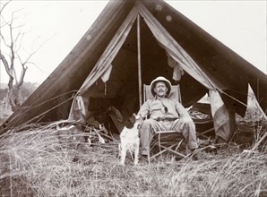 Frederick Stanbury outside a tent. Stanbury is seated on a canvas chair in front of a small open