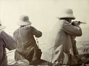 Shooting hippopotamus on Lake Victoria. A back view of three European men aiming at hippopotami