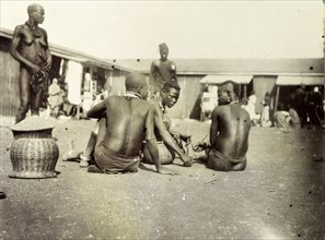Luo men and women at Kisumu market. Luo men and women chat, seated on the ground outside a local