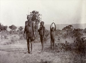 Luo woman and children carrying milk. A Luo women and her two children balance tall bottles of milk