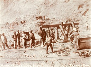 Convicts labouring at a diamond mine. African convicts on loading duty with a European overseer at