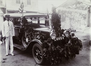 Remembrance Day car. An African chauffeur stands beside a car decorated with foliage and Union