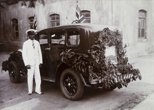 Remembrance Day Car. An African chauffeur stands beside a car decorated with foliage and Union