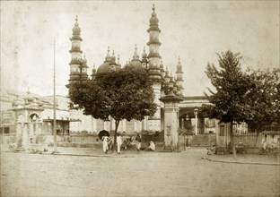 Mosque on Dhurumtollah Street. People sit in the shade of trees outside a mosque decorated with