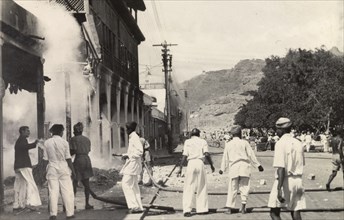 Relief work after the Arab riots in Aden, 1947. Teams of men use two hose pipes to douse the flames